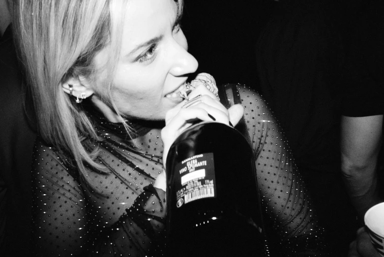 a woman is drinking from a bottle while sitting in a bar