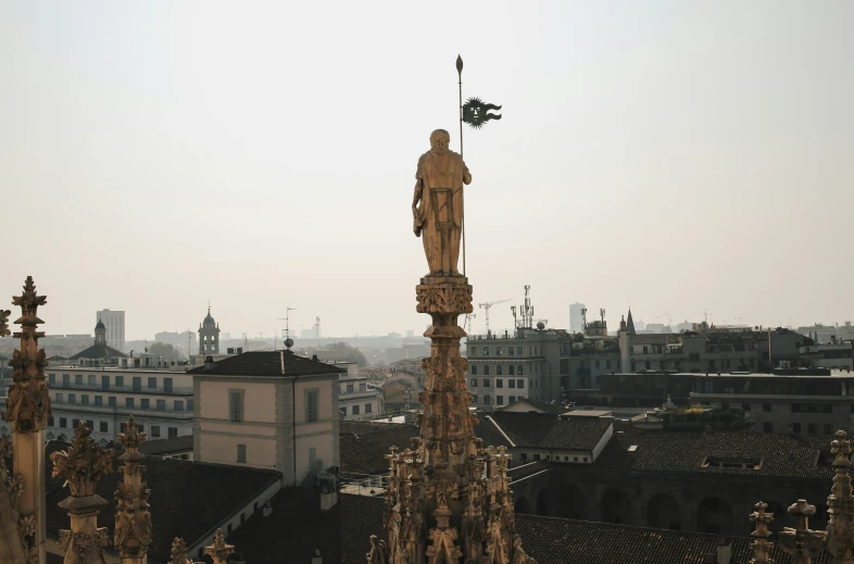 a statue stands above a cityscape in the distance