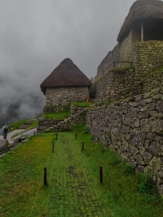 two people walking up the side of a hill near a stone wall