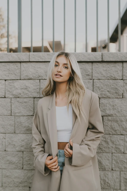 blond woman wearing gray jacket standing in front of a brick wall