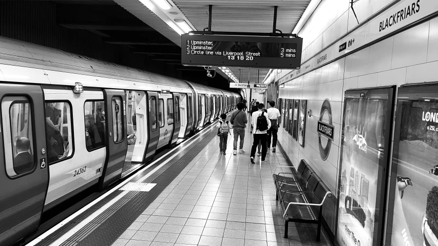 three people are walking along a long corridor between a subway car and a passenger train