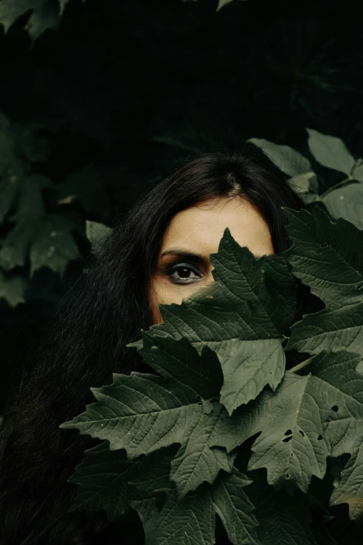 the woman with long hair is hiding behind the leaves
