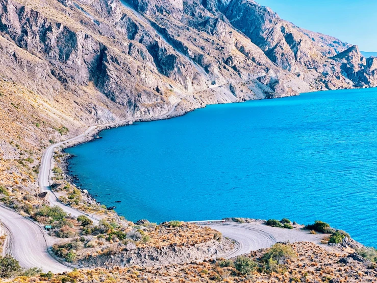 a road that is going through the mountains by water