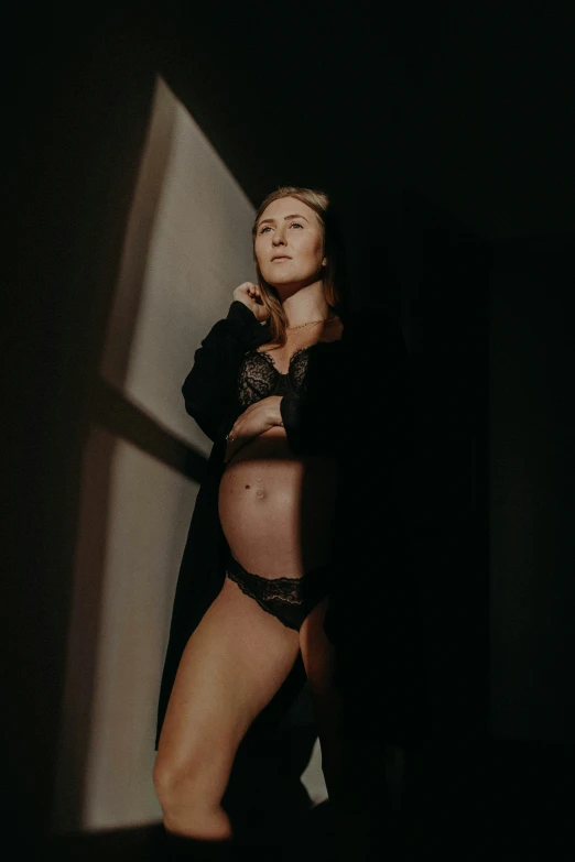a pregnant woman in lingerie standing near wall