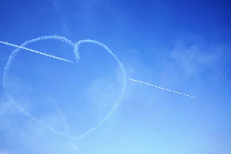 a heart shaped contrail in the sky and there are two jets that are passing