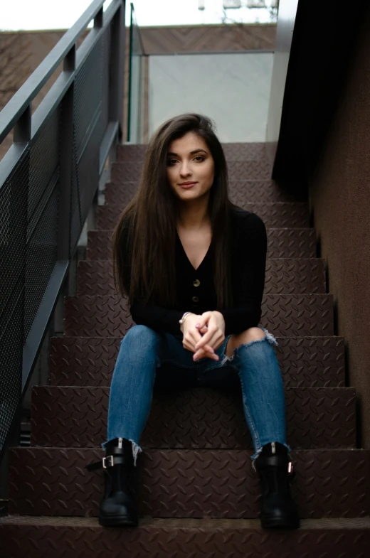 an attractive woman in black shirt and jeans sitting on stairs