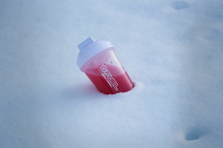 a cup of pink soda is partially frozen on the ground