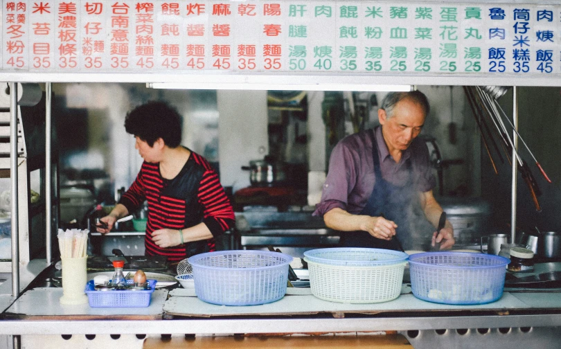 a person cooking behind a counter next to another person