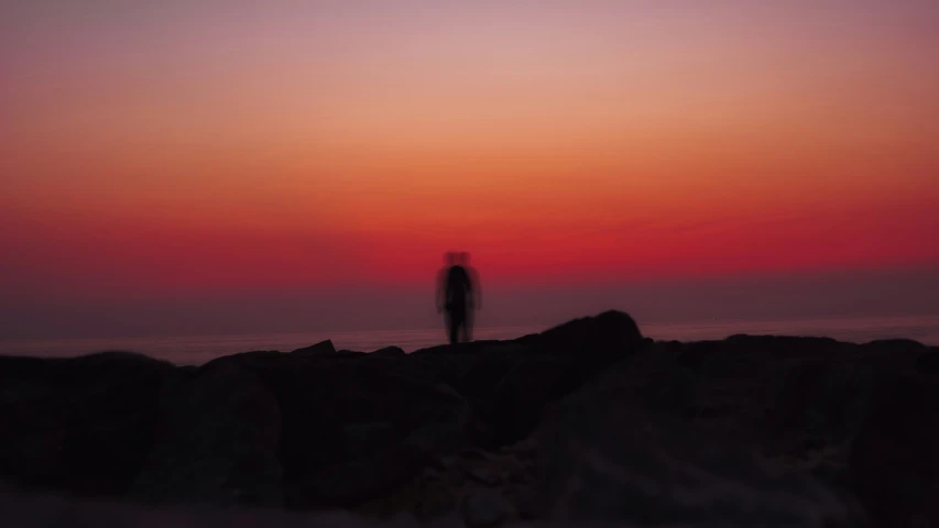 the person in silhouette is on rocks watching the sunset