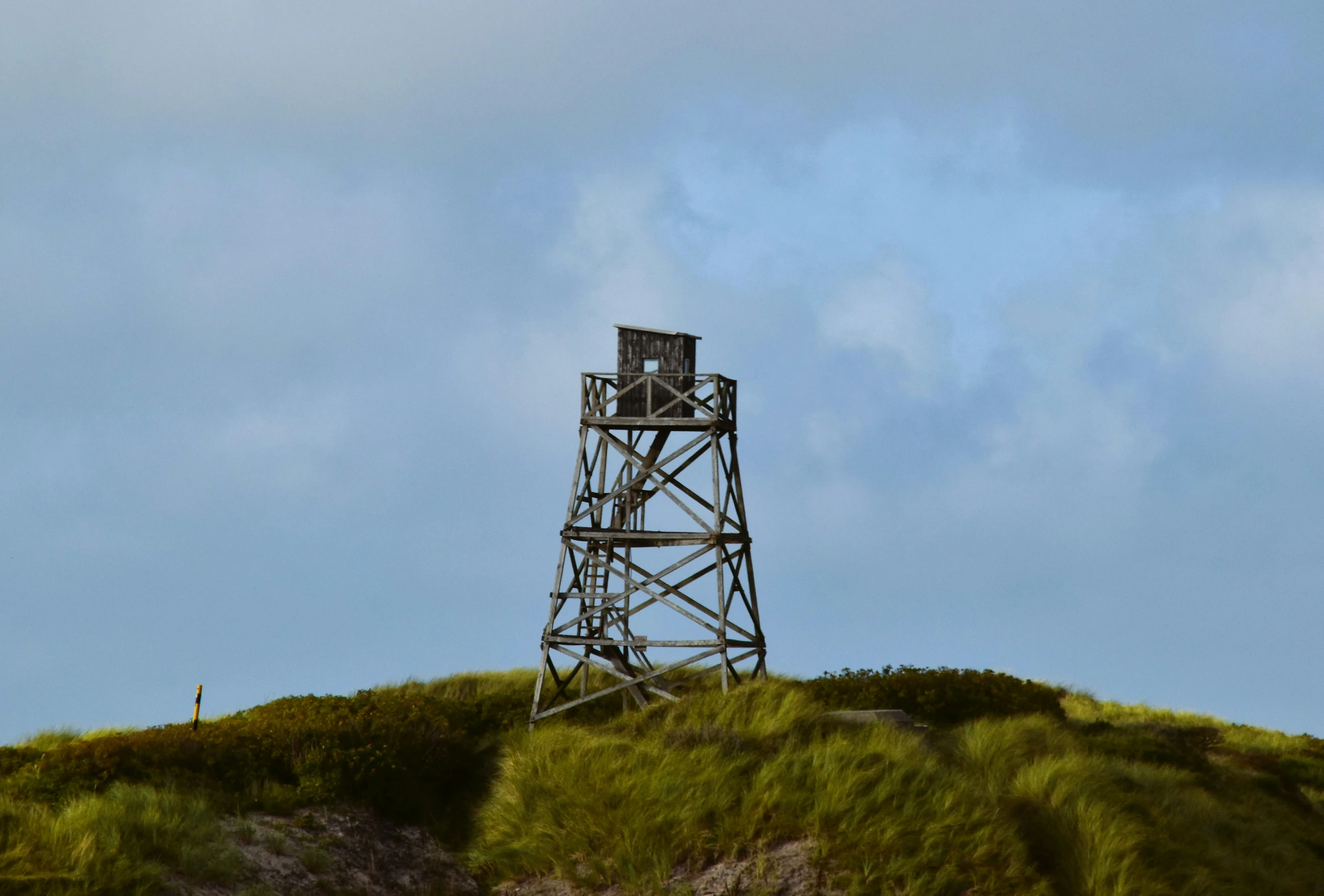 a fire tower atop a green hill with sky