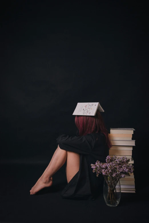 a woman sitting down wearing a hat, a book and a vase of flowers