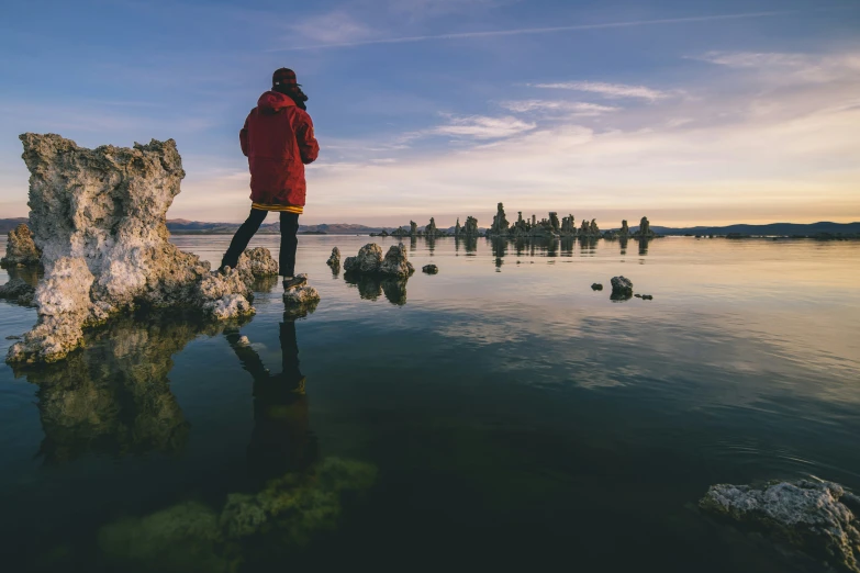 woman in red jacket standing next to large rock and body of water