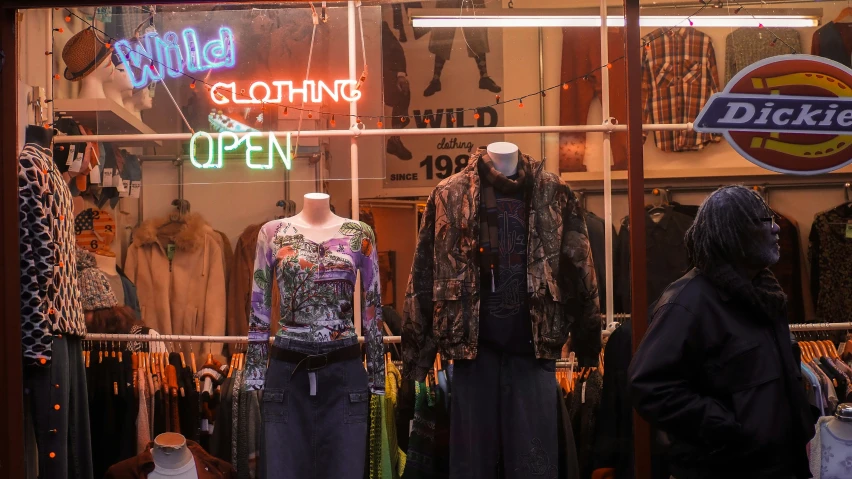 some mannequins in a clothing shop window with neon signs