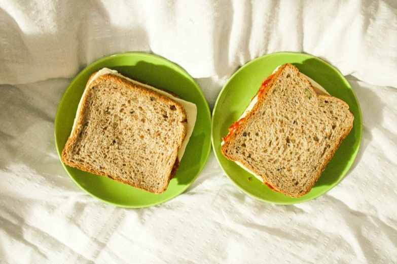 two green plates containing sandwiches and sauce on white sheets