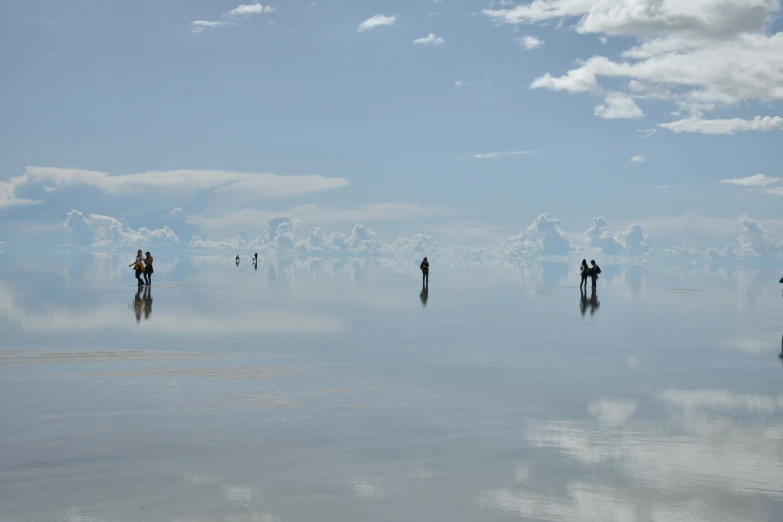 a beach with some people walking along the shore and clouds in the sky