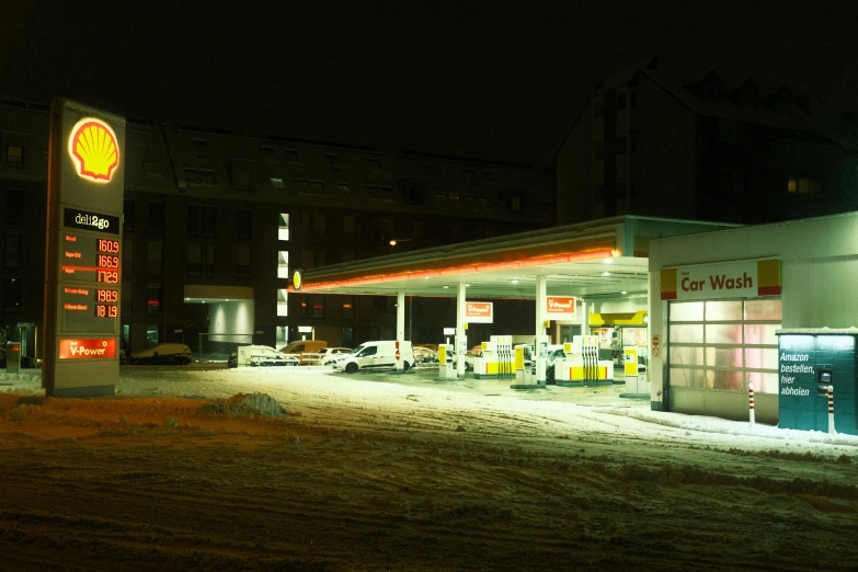 an oil station is lit at night with cars parked