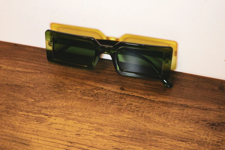 pair of dark green sunglasses resting against wooden wall