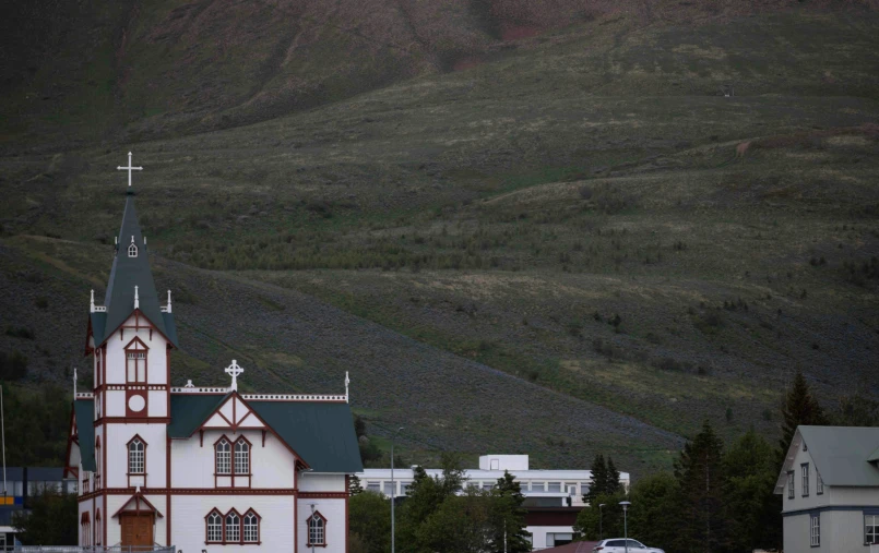 a church is in front of mountains with trees on the hill side