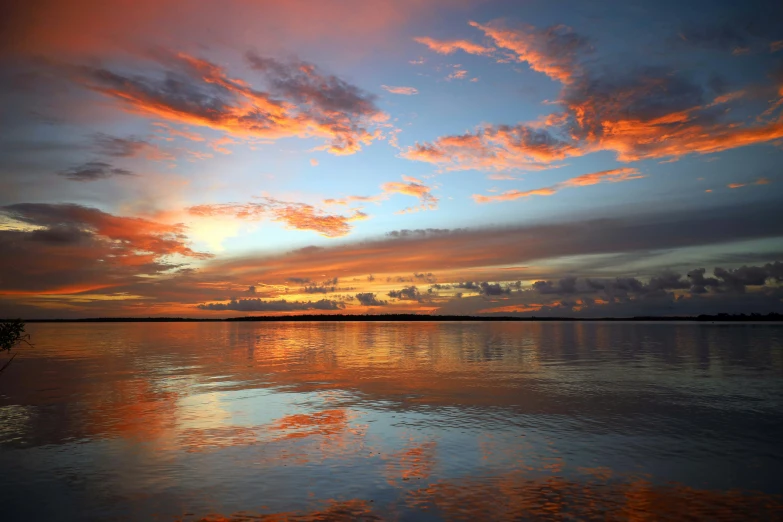 a boat in a lake that is reflecting a sky full of clouds