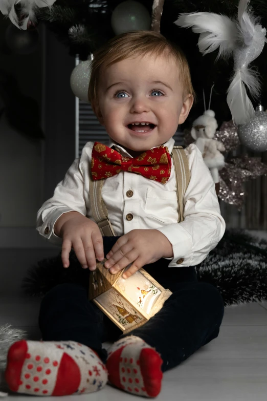 a baby wearing an odd looking bow tie playing with a box