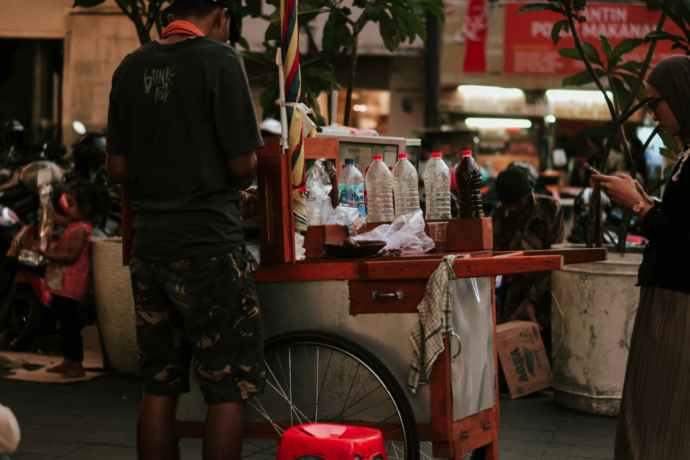 two people standing in front of a cart selling bottles of alcohol