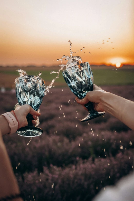 two people's hands are holding wine glasses in front of the sunset