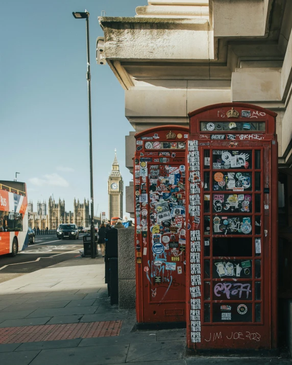 two telephone booths sitting outside a building with some stickers on them