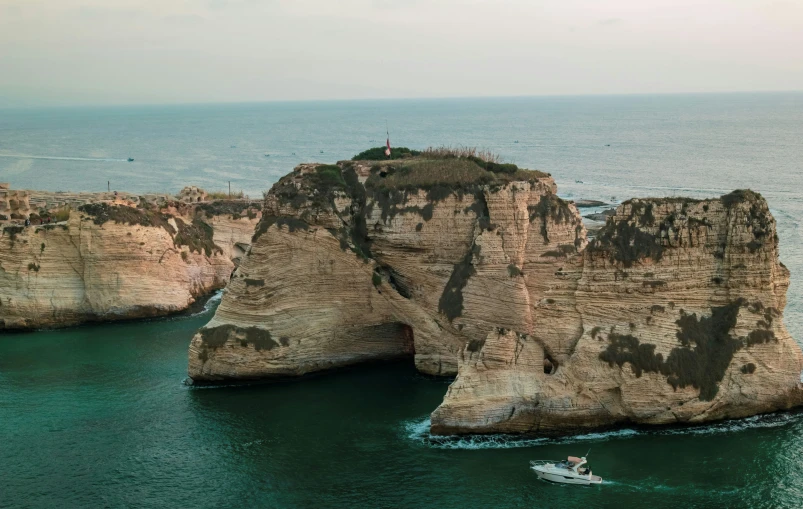 boat floating by a large rock formation at the ocean