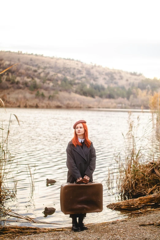 woman sitting by a lake holding a suitcase