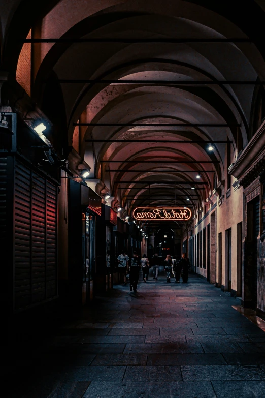 people walking down an arched walkway at night