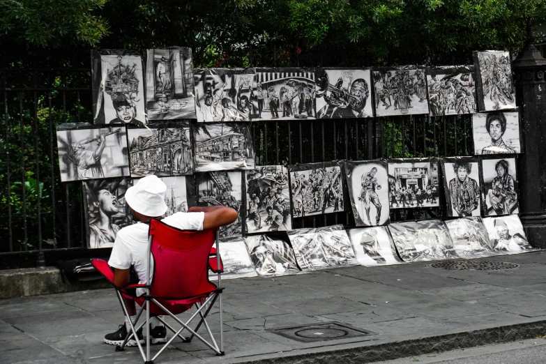 a person is sitting in a chair near a fence covered in black and white paper