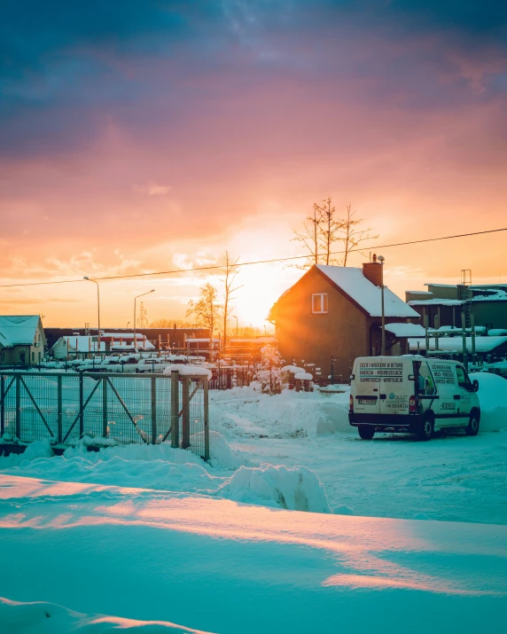 the sun is setting over some houses on the snow