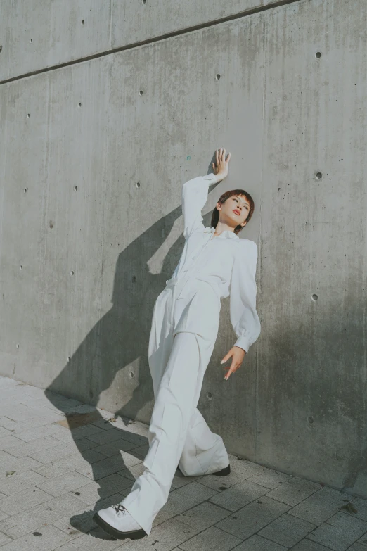 a young woman poses in front of a wall while wearing all white