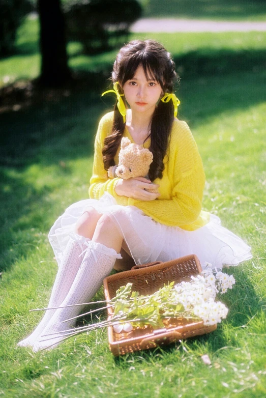 a girl is sitting in the grass holding a teddy bear