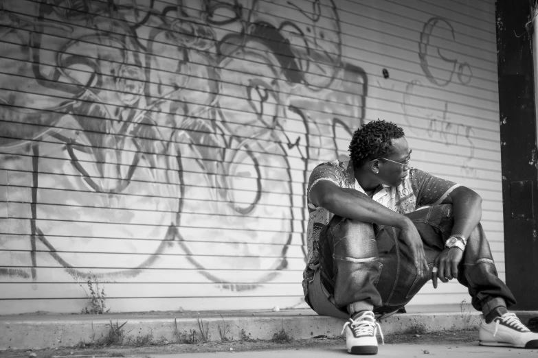 a man sitting on the side walk by graffiti