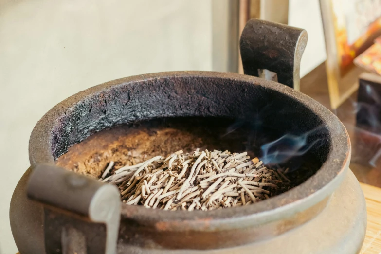 an old fashioned cooking pot with sticks and some dirt in it