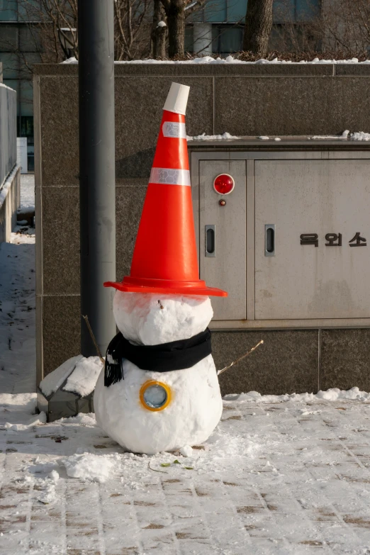 a snowman wearing a traffic cone on the sidewalk