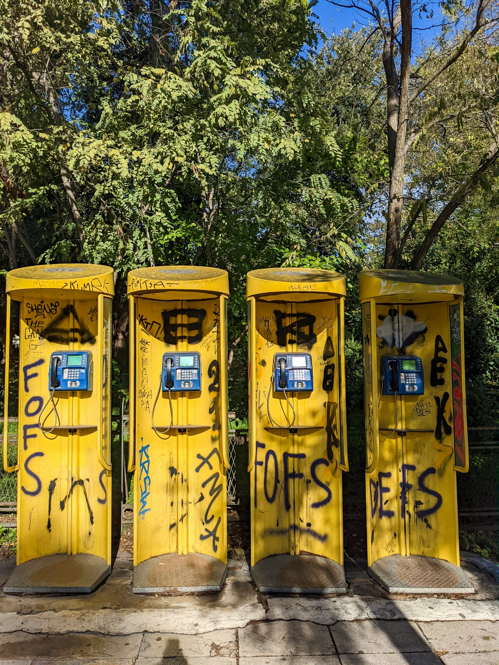 three yellow phone booths sitting in front of a tree