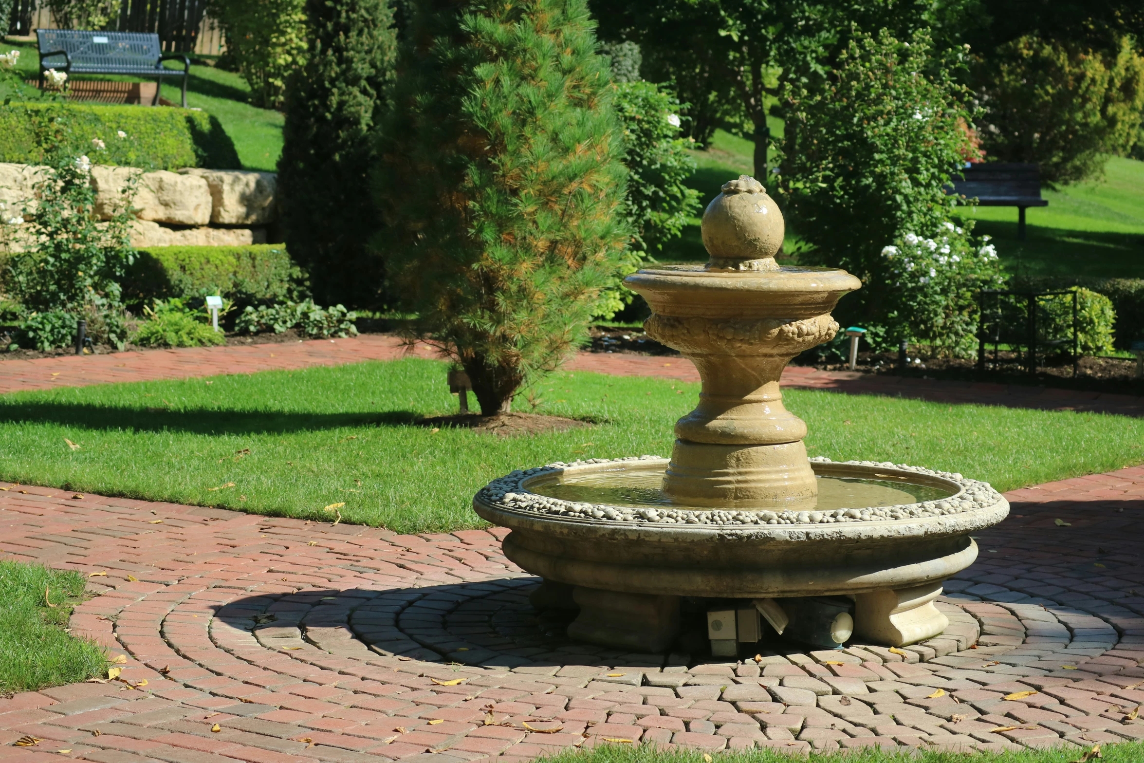 a stone water fountain sits on a path next to some grass