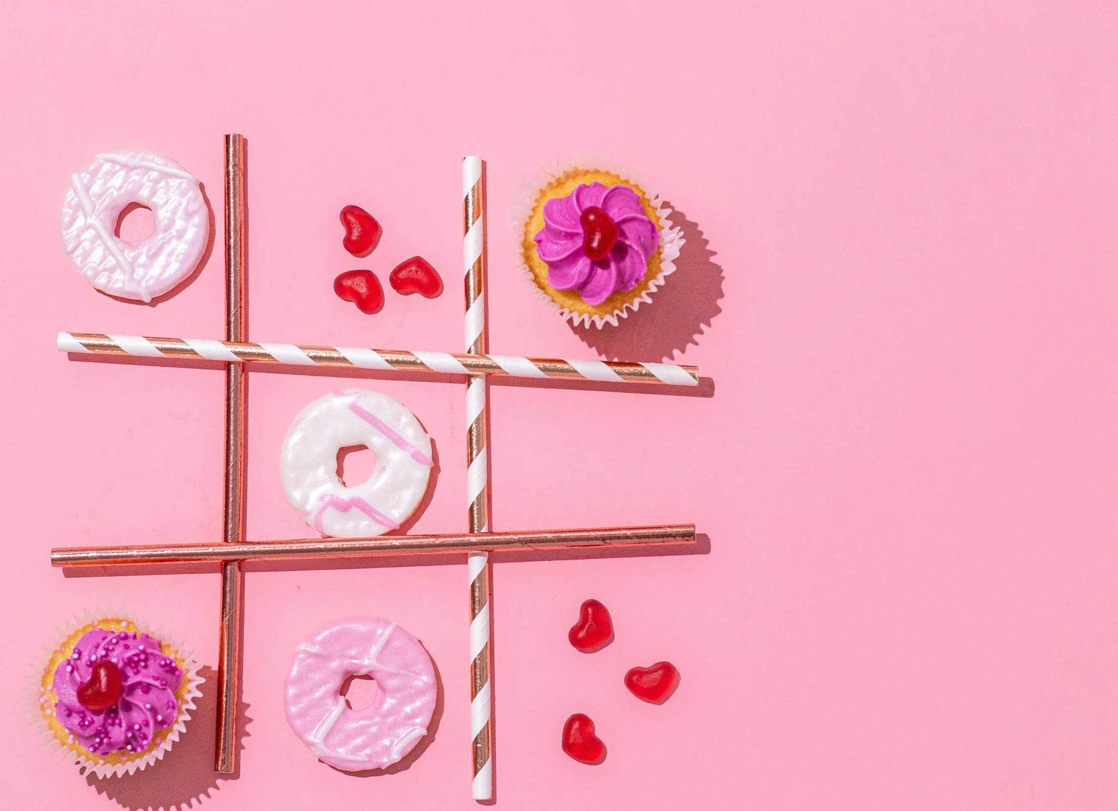 two lollipop sticks, cupcakes and chocolate hearts are arranged over a pink background