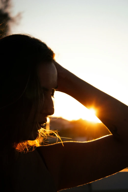 there is a woman standing in the sun with her hands to her head