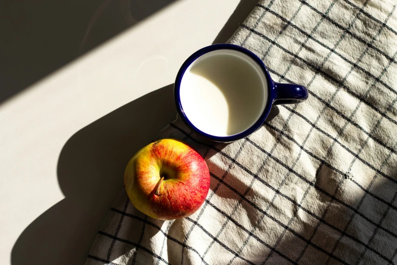 an apple, cup of milk, and cloth sit on a table