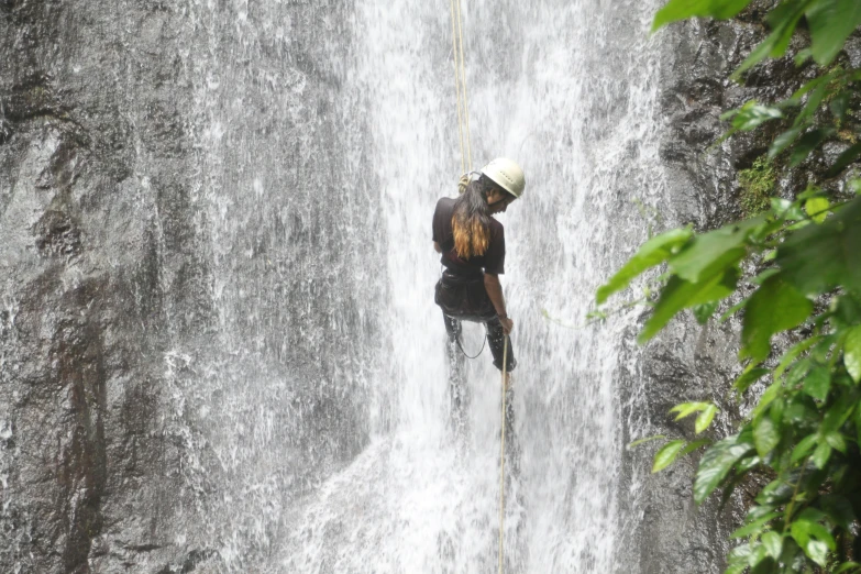 a man hanging on to a rope near waterfall