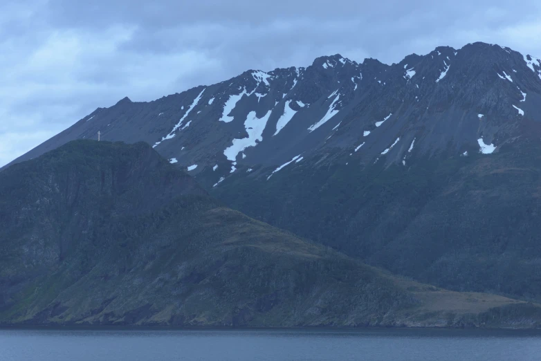 a big mountain covered in snow sitting on the side of a body of water