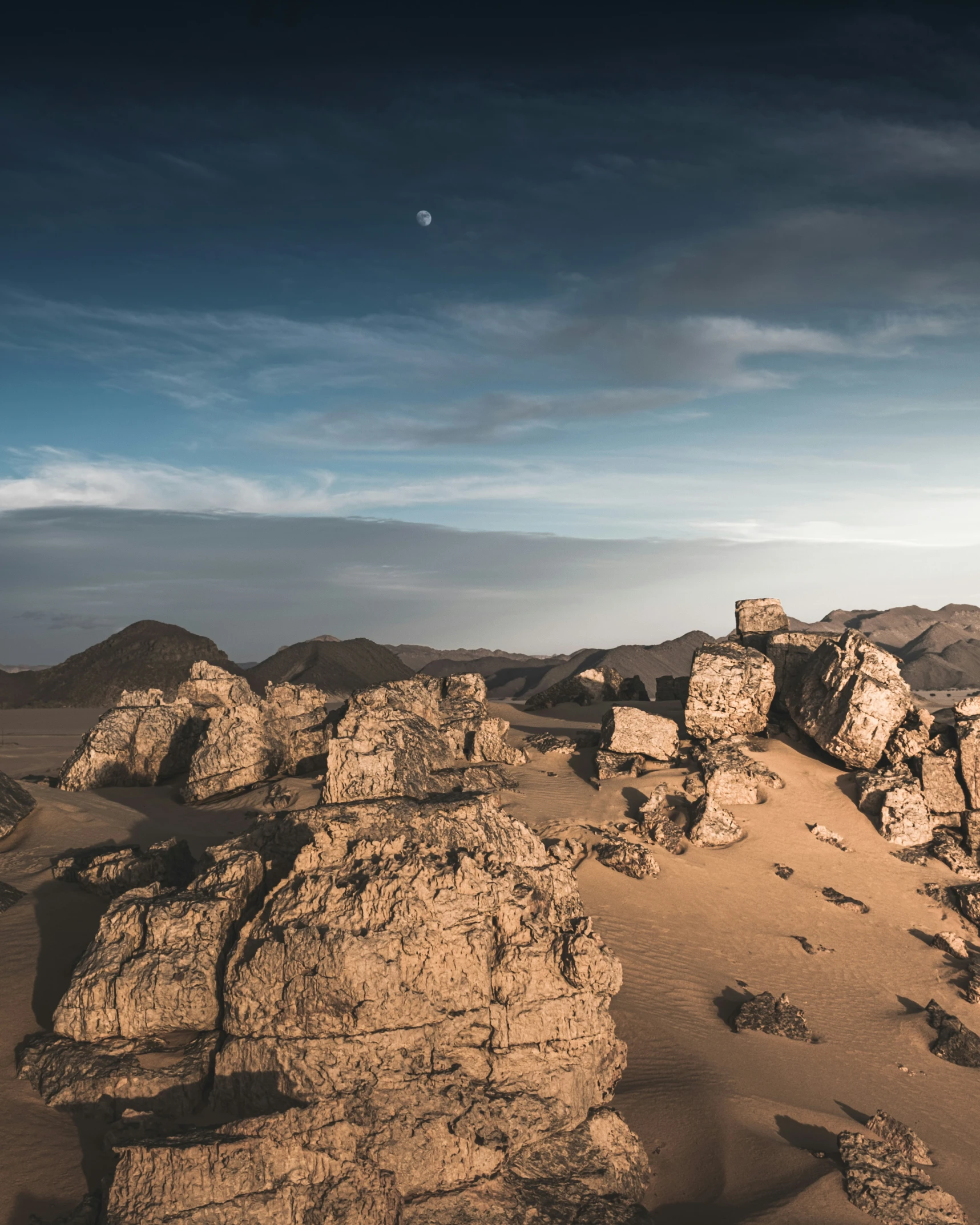 some rocks and hills with an moon behind it