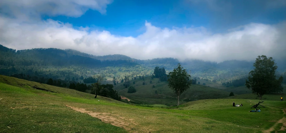 people resting on the grass overlooking a hilly valley