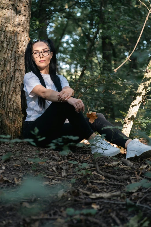 a woman sits on the ground near a tree