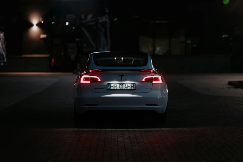 the back end of a white car parked in the dark