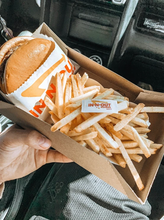 someone holding a box of french fries and burger