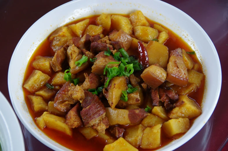 a bowl of food containing meat, potatoes and tomatoes